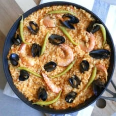 seafood paella in a large black skillet, on top of a blue and white tea towel.