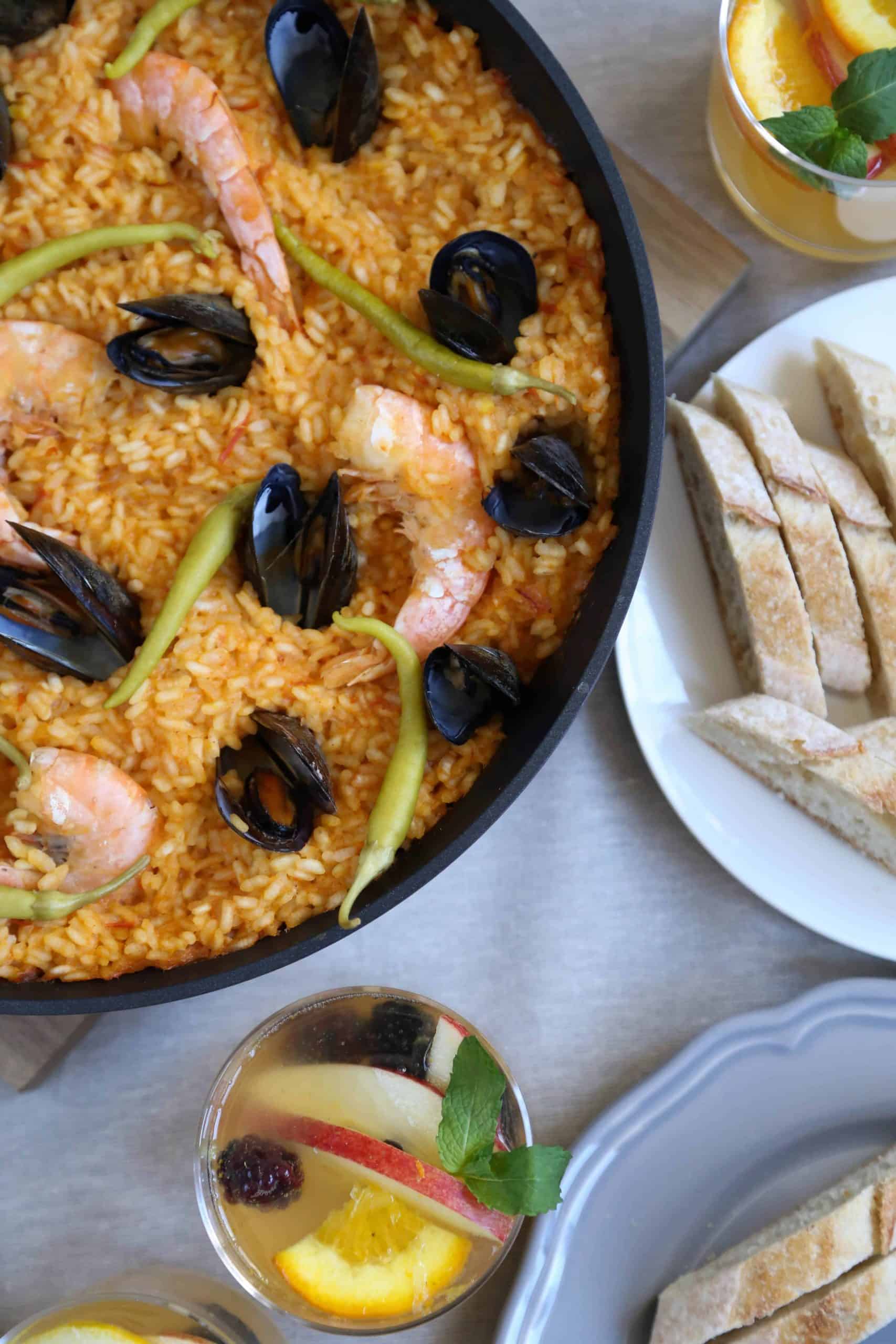 pan of seafood paella on a table with sliced bread and a glass of sangria.