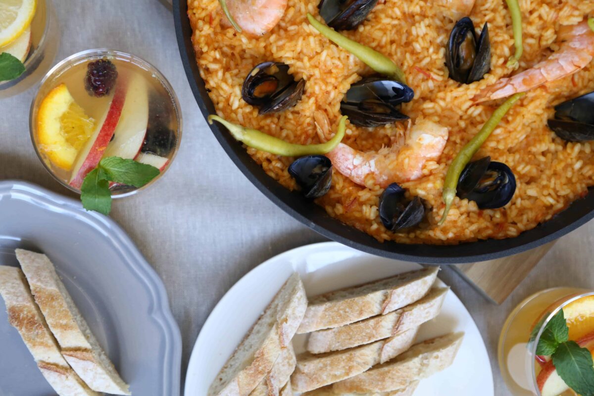 dinner table set with paella, sangria, and sliced baguette.