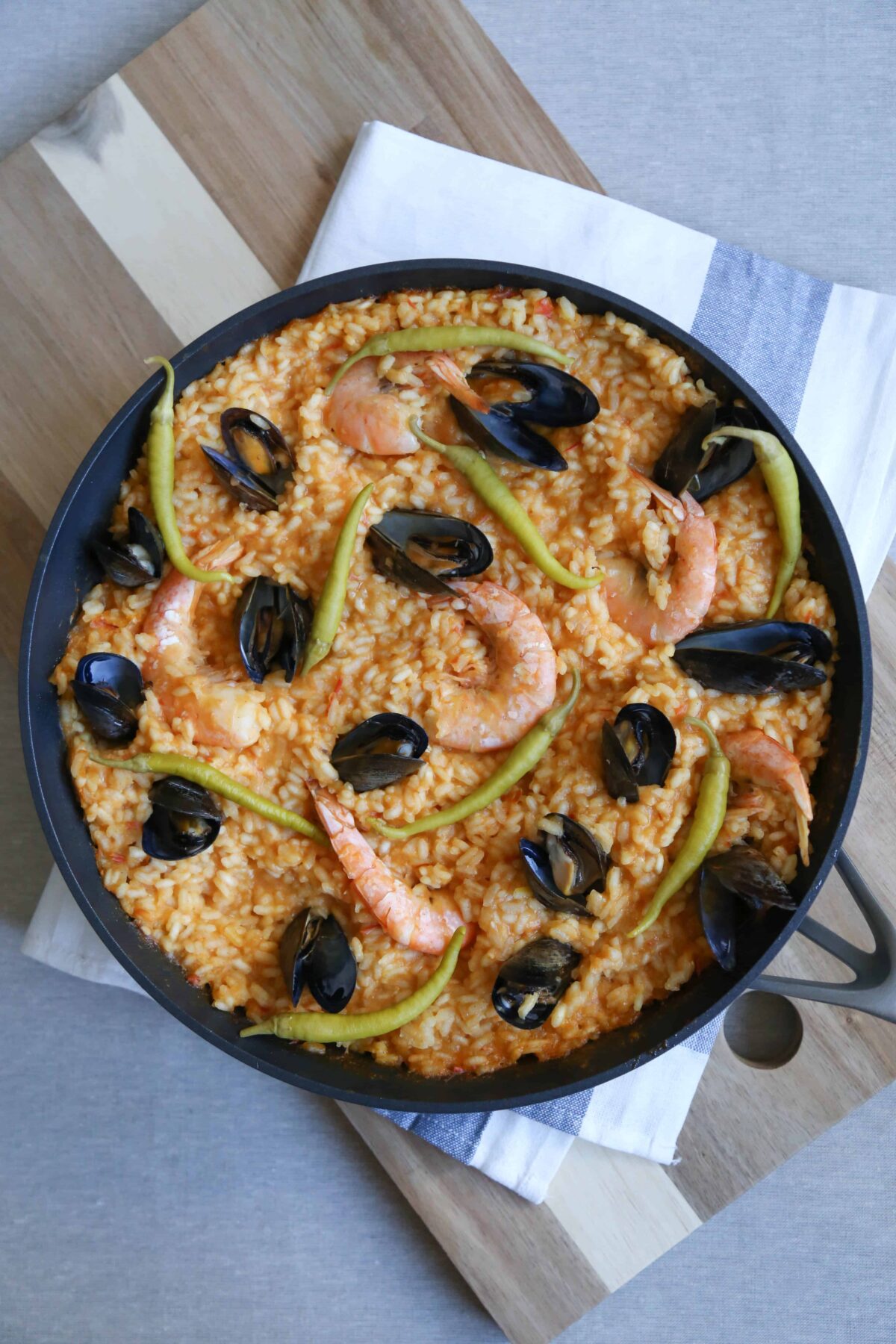 seafood paella in a black pan on top of a tea towel and wooden cutting board.