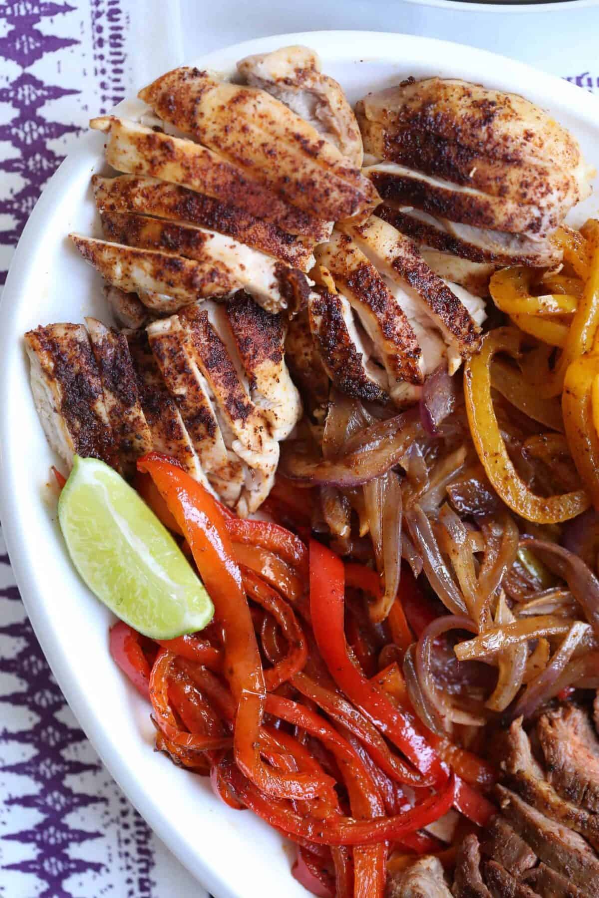 white platter with bell peppers, onions, chicken, and steak