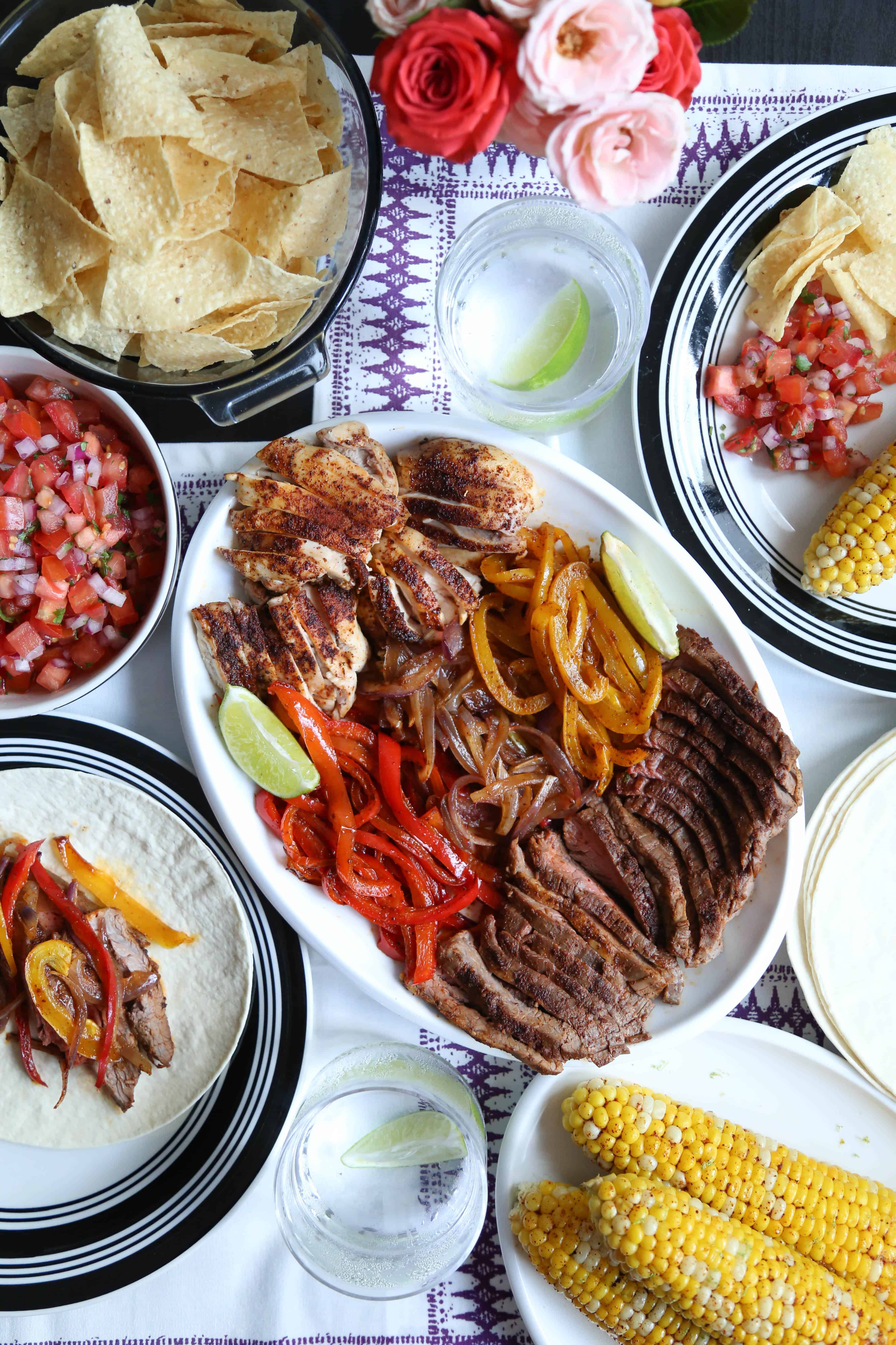 steak and chicken fajitas on a white platter on a dinner table.