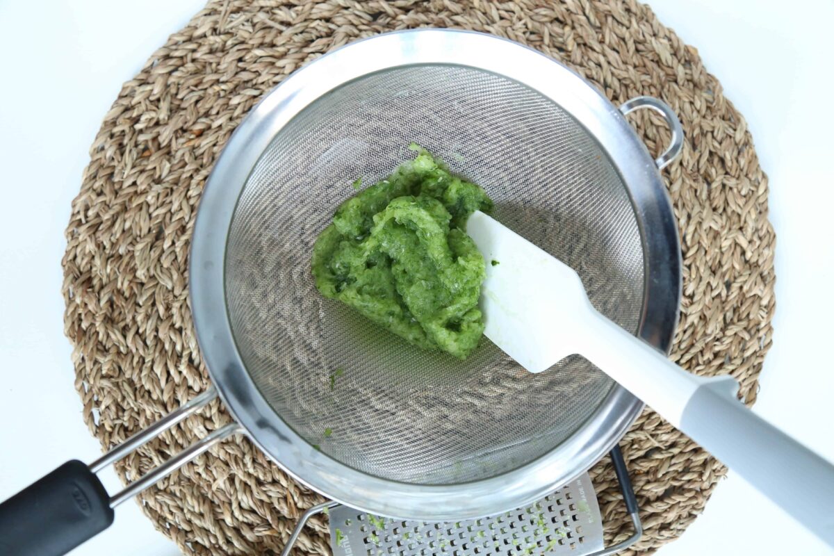 spatula pressing grated cucumber into a mesh colander