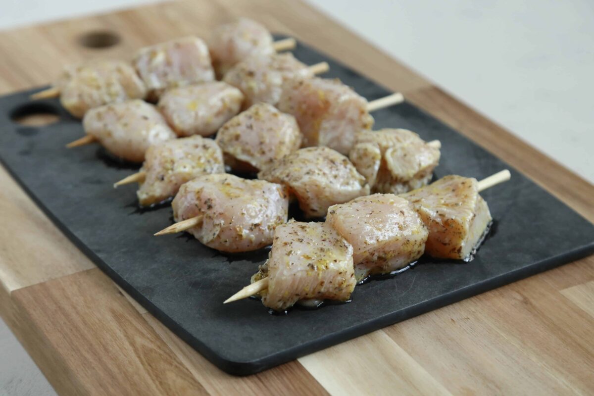 raw chicken skewers on a black cutting board.