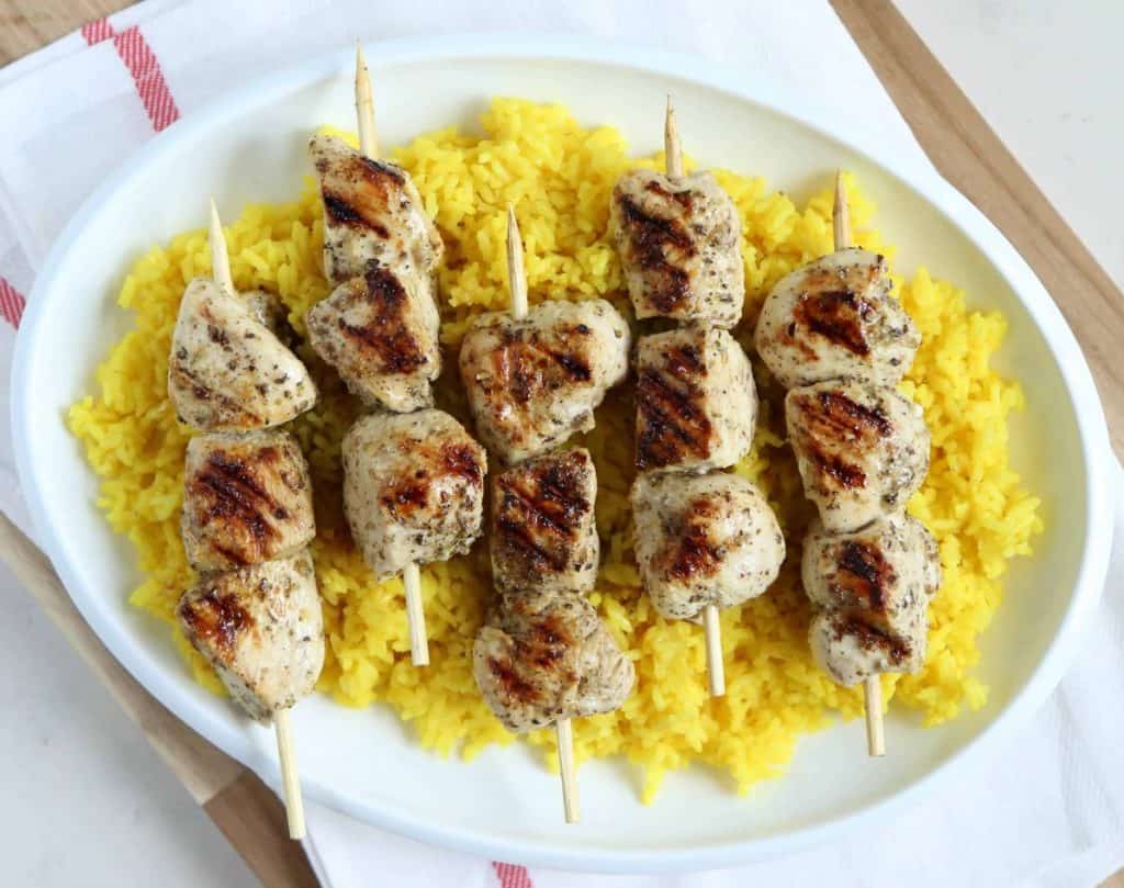 chicken souvlaki and golden rice on a white platter, sitting on a white tea towel