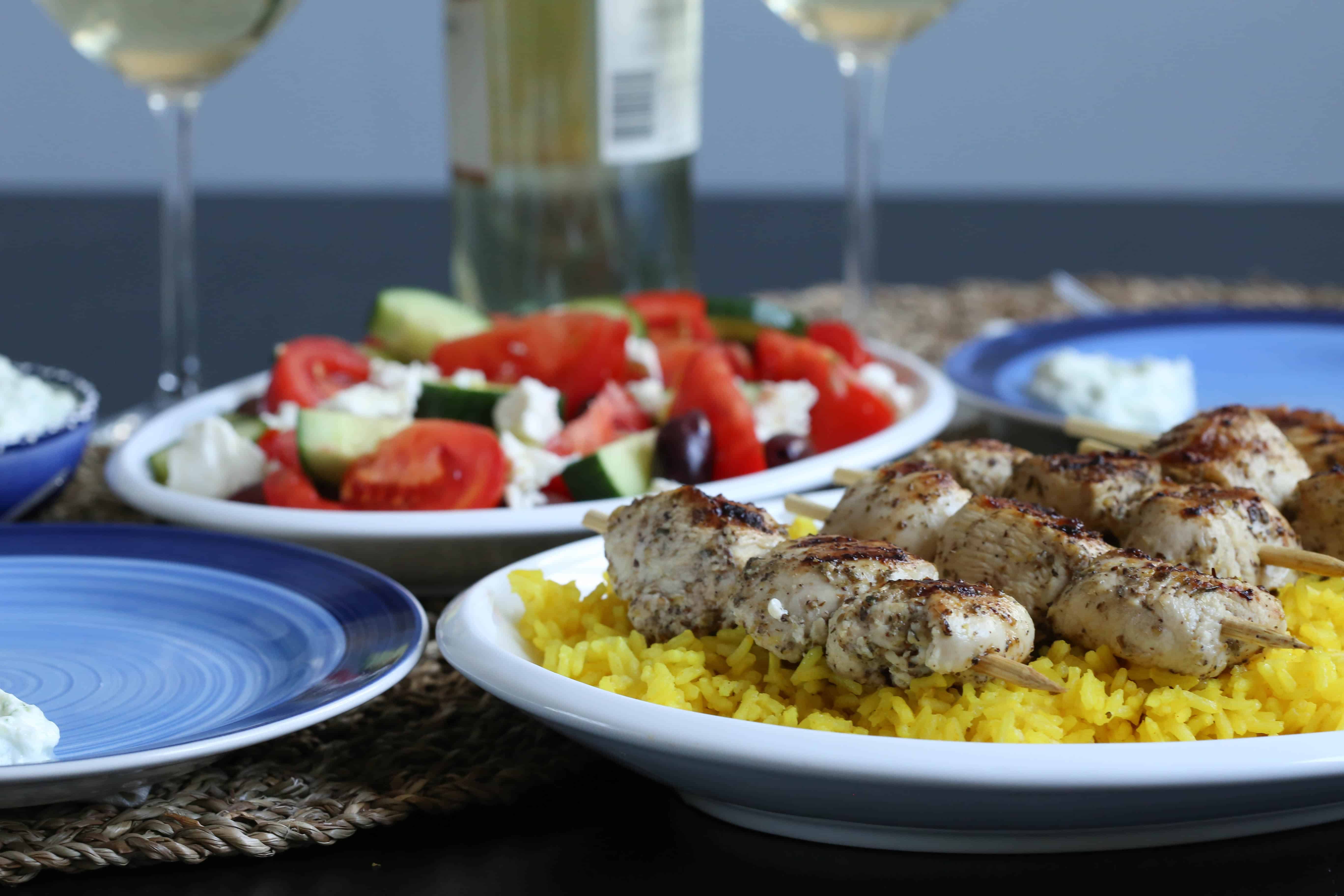 rice, chicken kabobs, and greek salad on a dinner table with plates and wine glasses.