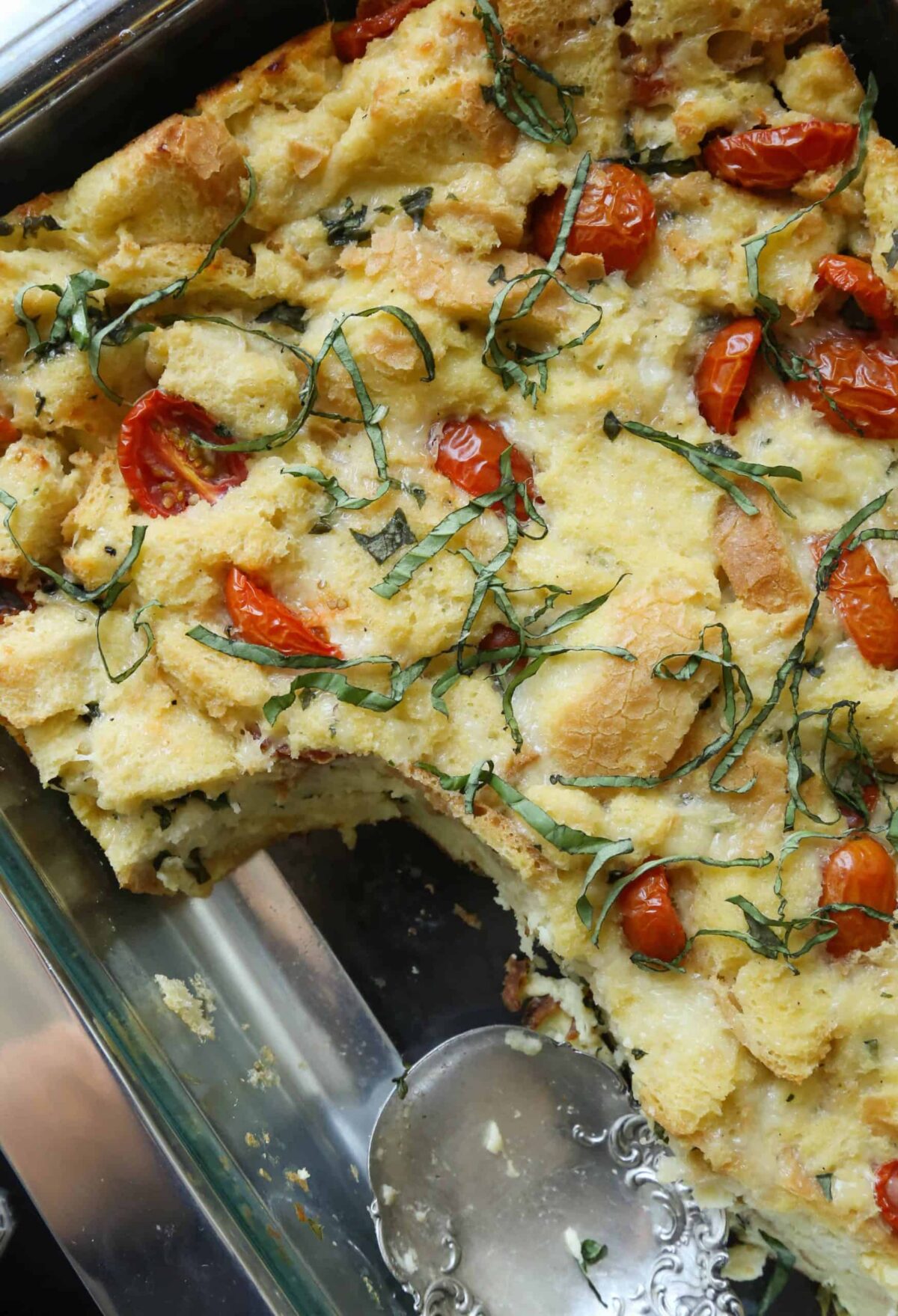 glass casserole dish filled with caprese bread pudding, with a scoop taken out.