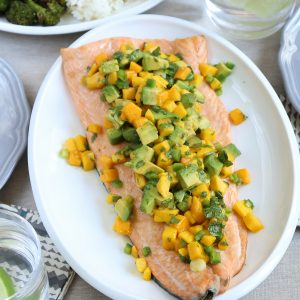 side of salmon on a white platter, topped with a mango and avocado salsa.