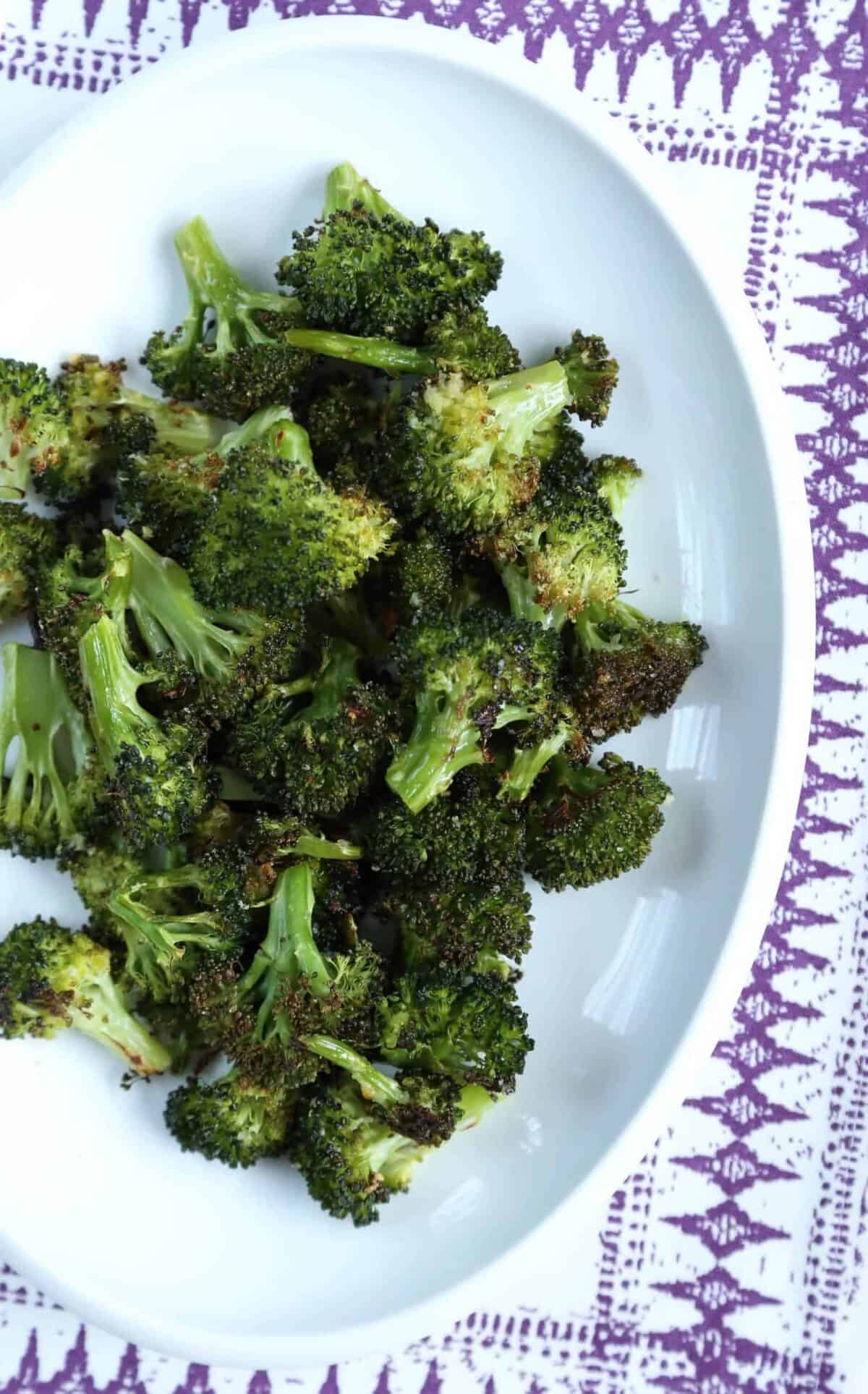 roasted garlic broccoli on a white platter on top of a white and purple placemat.