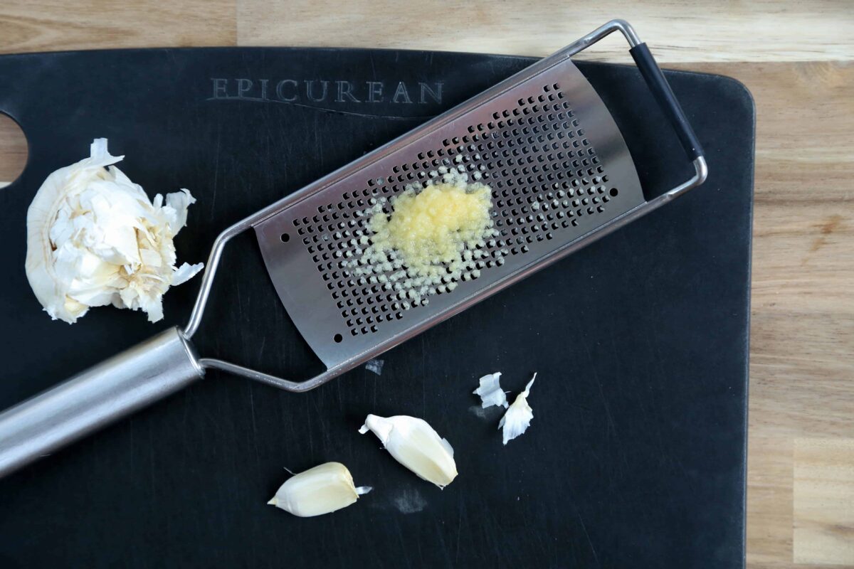 cloves of garlic next to a microplane with grated garlic on it.