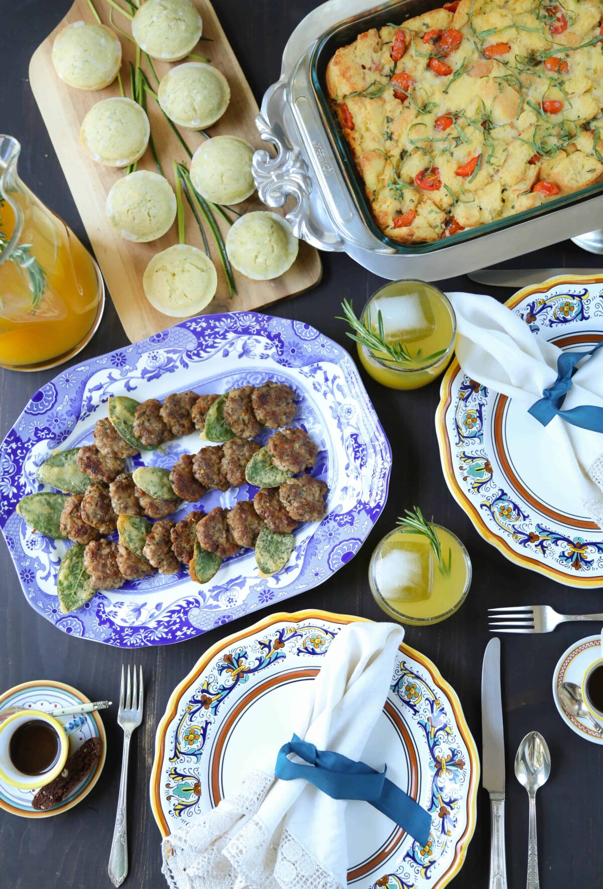 table set for brunch with sausage patties, egg casserole, muffins, and clementine cocktails.