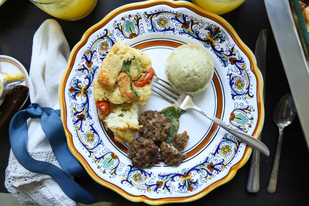 decorative china plate filled with caprese bread pudding, a muffin, and sausage patties.