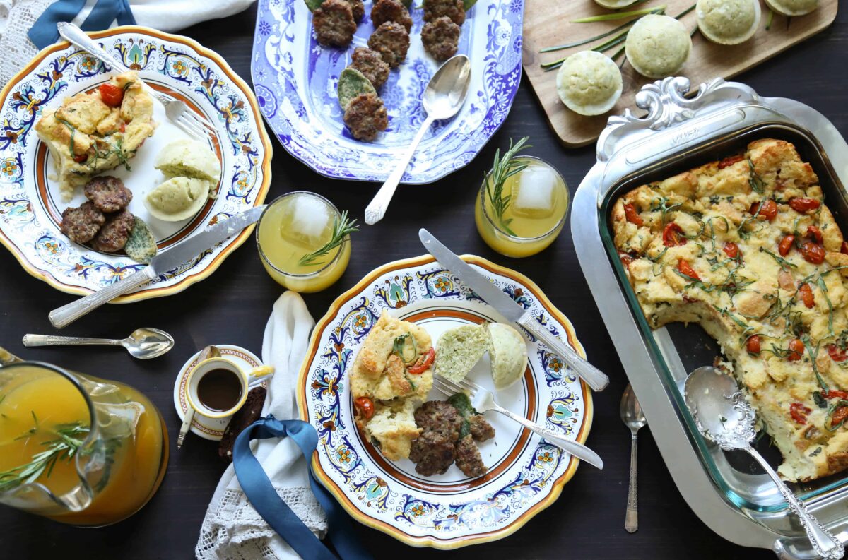 table set for brunch with italian china, caprese bread pudding, muffins, sausage patties, orange cocktails, and espresso in mini cups.