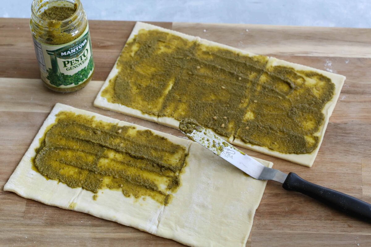 puff pastry on a wooden board topped with pesto.