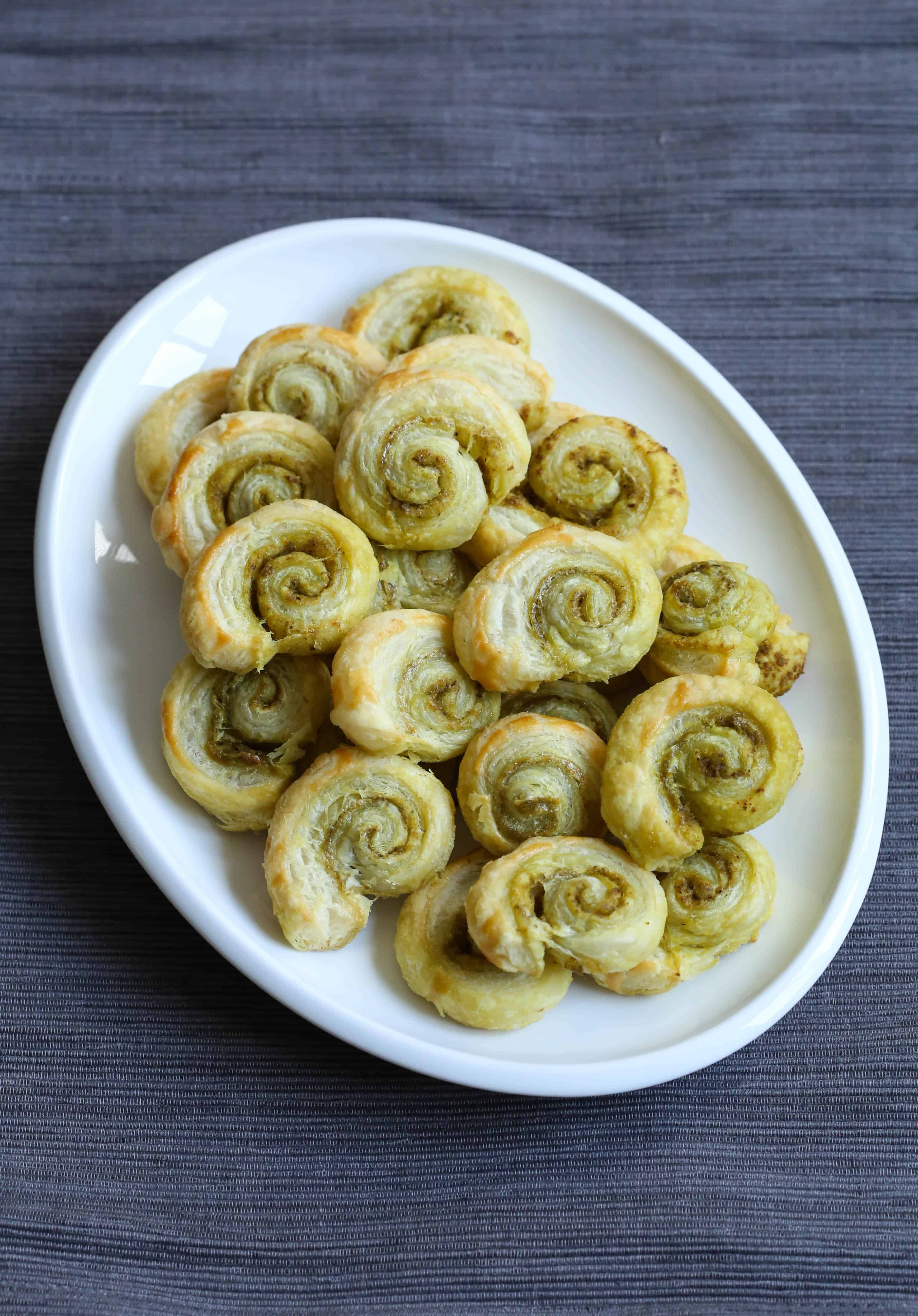 Pesto pinwheels on a white platter sitting on a gray placemat.