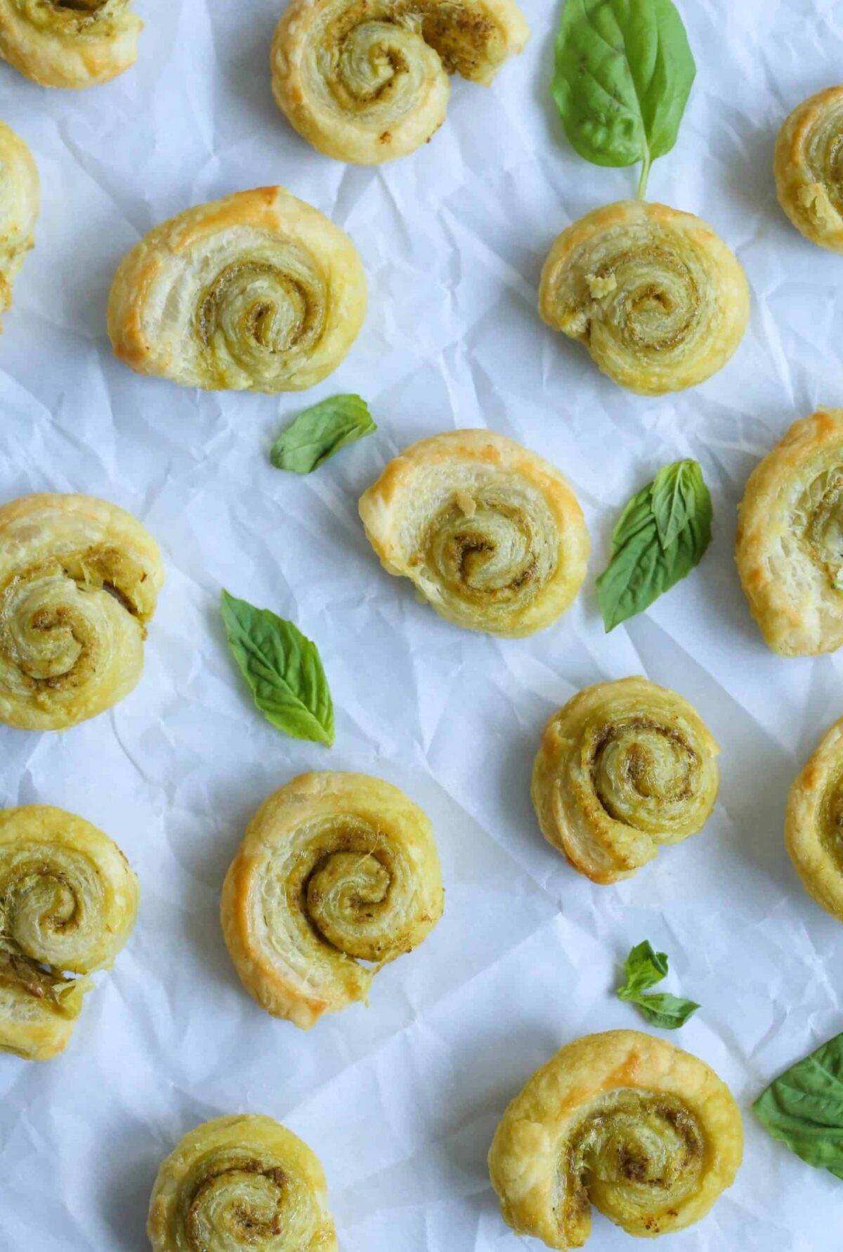 pesto pinwheels and basil leaves on a sheet of white parchment paper.