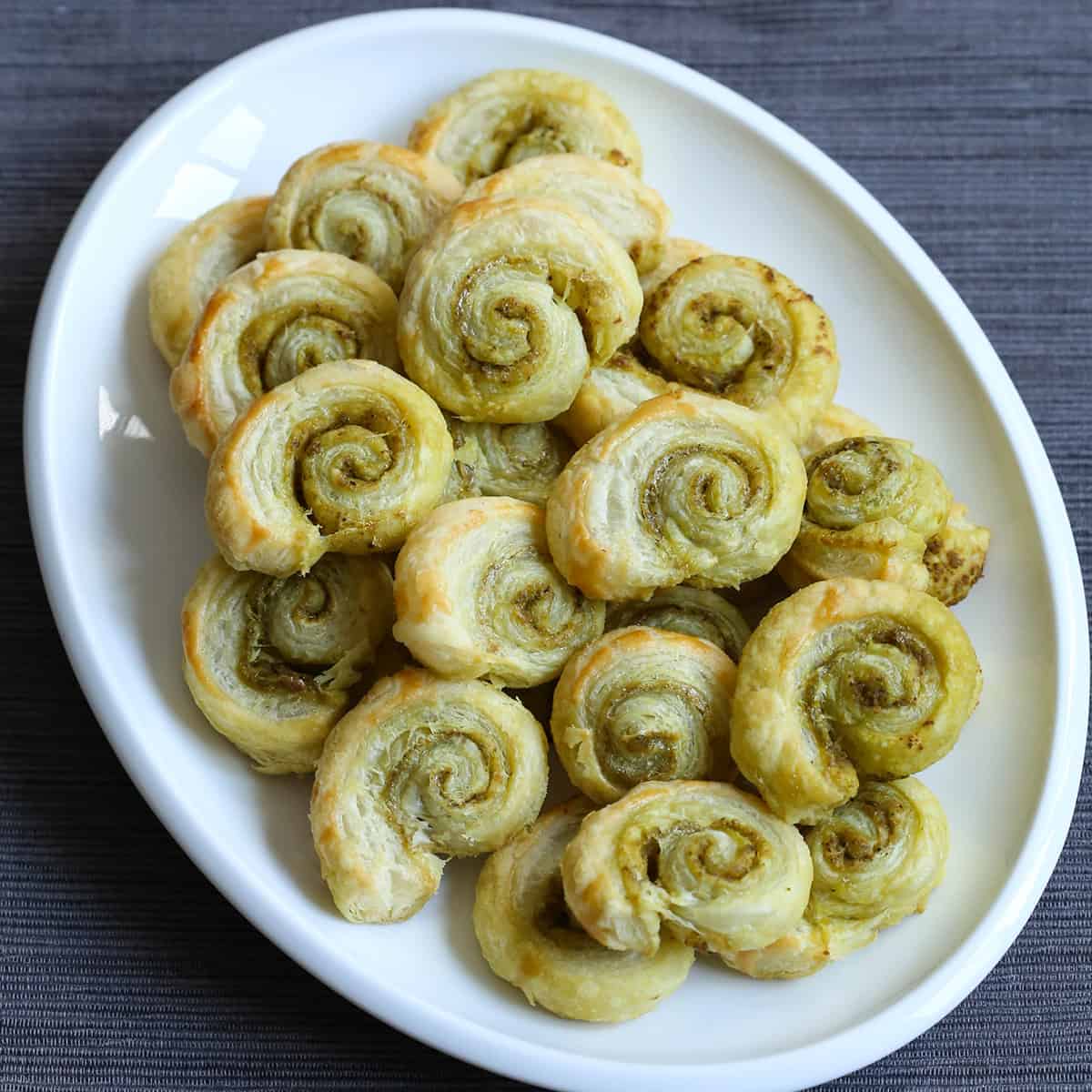 pesto pinwheels on a white platter sitting on a gray tablecloth.