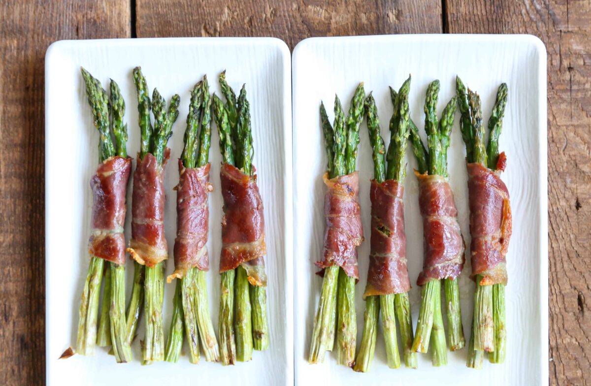 cooked prosciutto wrapped asparagus bundles on white platters.