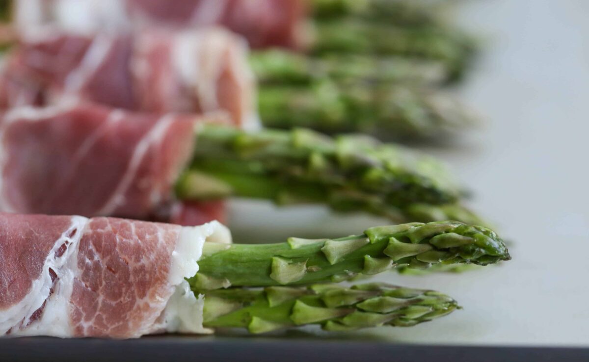 close-up of uncooked prosciutto wrapped asparagus on a sheet tray.