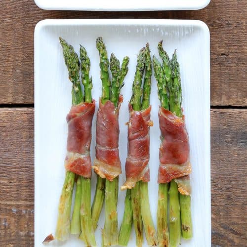 prosciutto wrapped asparagus on a white platter.