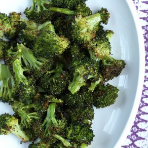 roasted broccoli on a white platter with a purple and white tablecloth underneath.