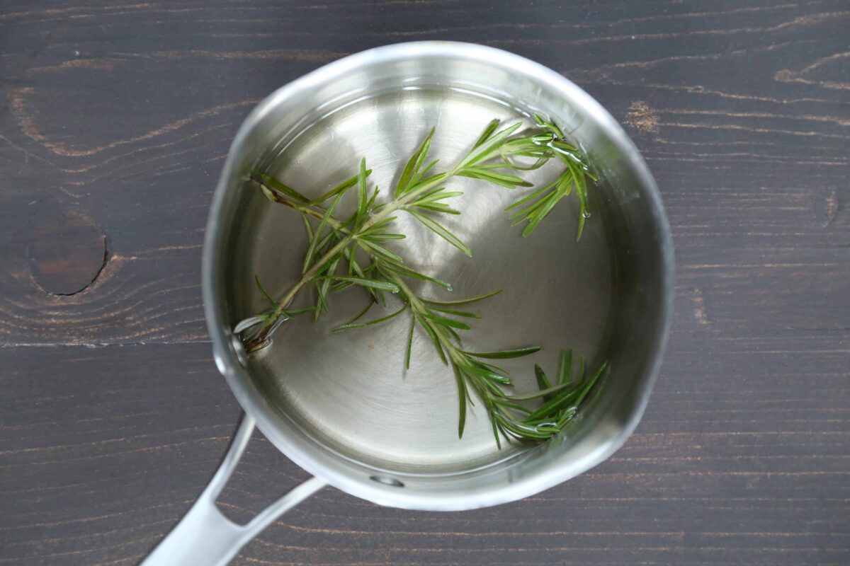 rosemary sprigs in simple syrup in a metal pan.