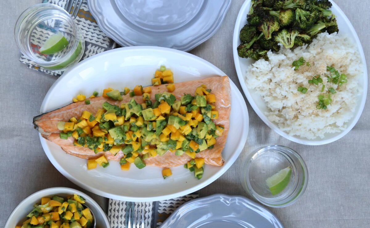 table set with gray dinner plates, an oval platter with salmon, and an oval platter with broccoli and rice.