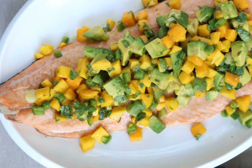 whole side of salmon with mango and avocado salsa on a white oval platter.