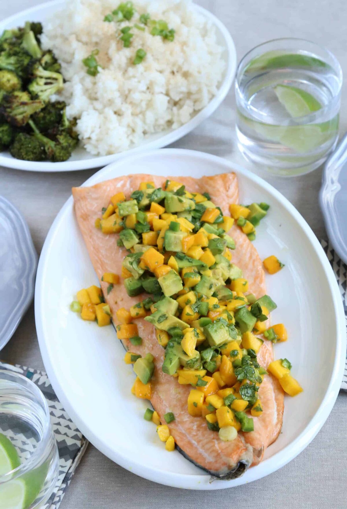 white platter with a side of salmon, topped with mango and avocado salsa, with rice and broccoli in the background.