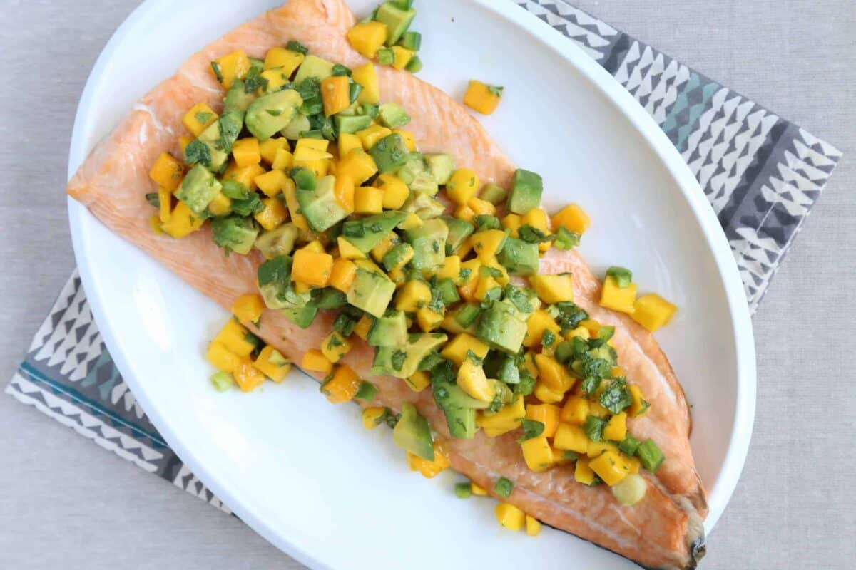 white platter with salmon topped with mango and avocado salsa.