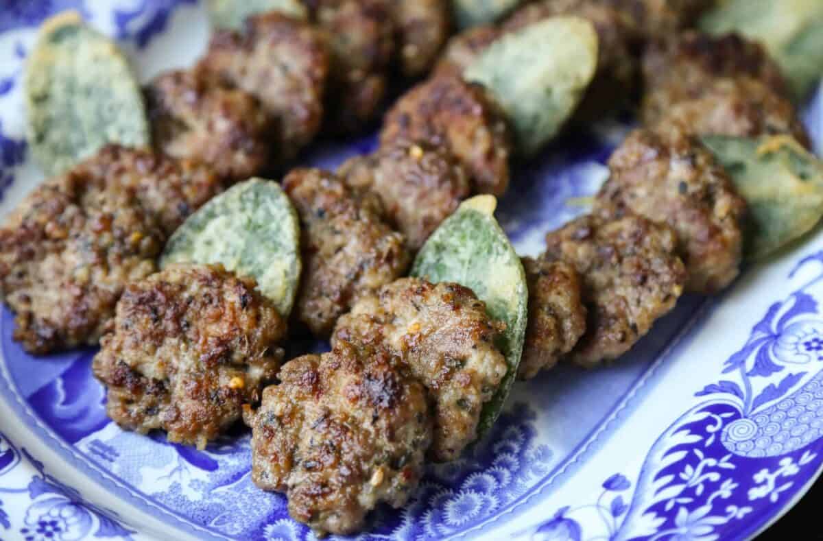 sausage patties and fried sage leaves on a blue and white platter.