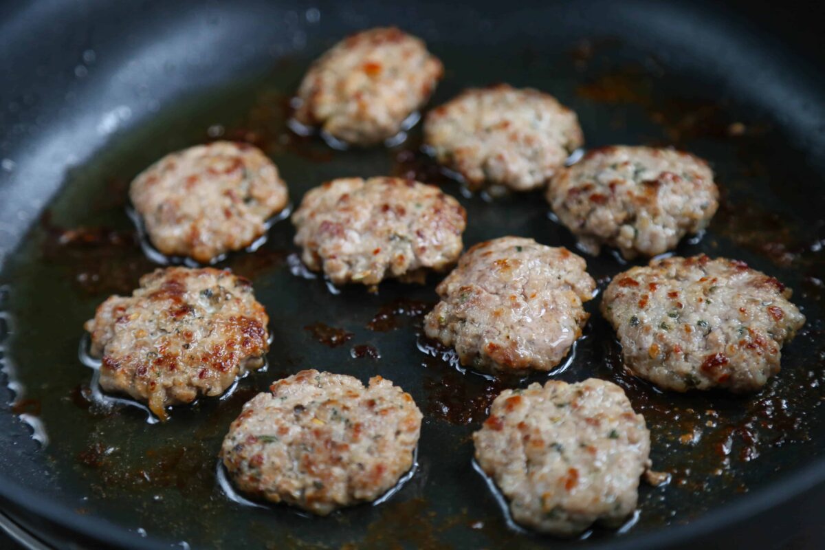 sausage patties cooking in a large black skillet.