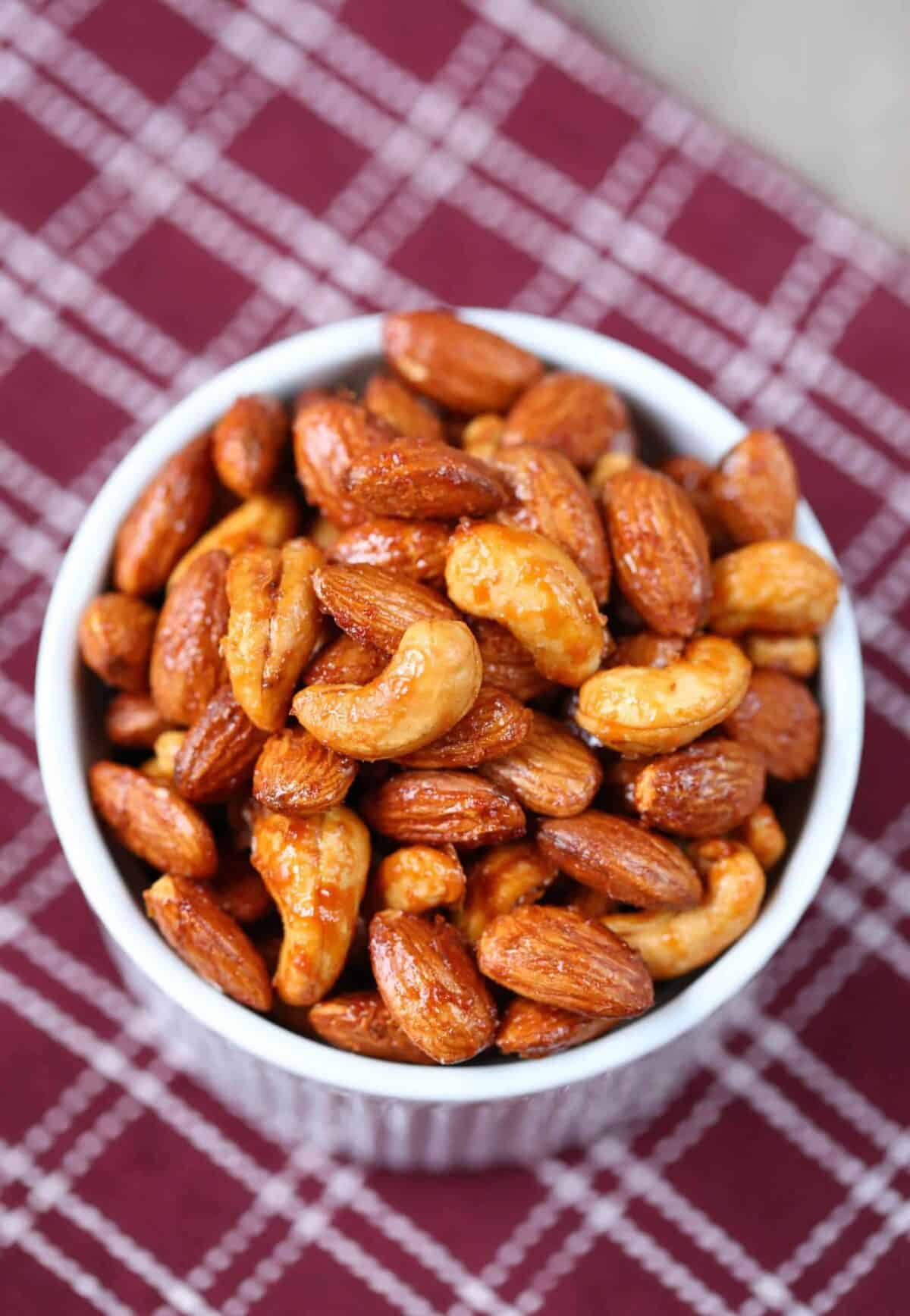 maple sriracha roasted nuts in a white dish on a burgundy tea towel.