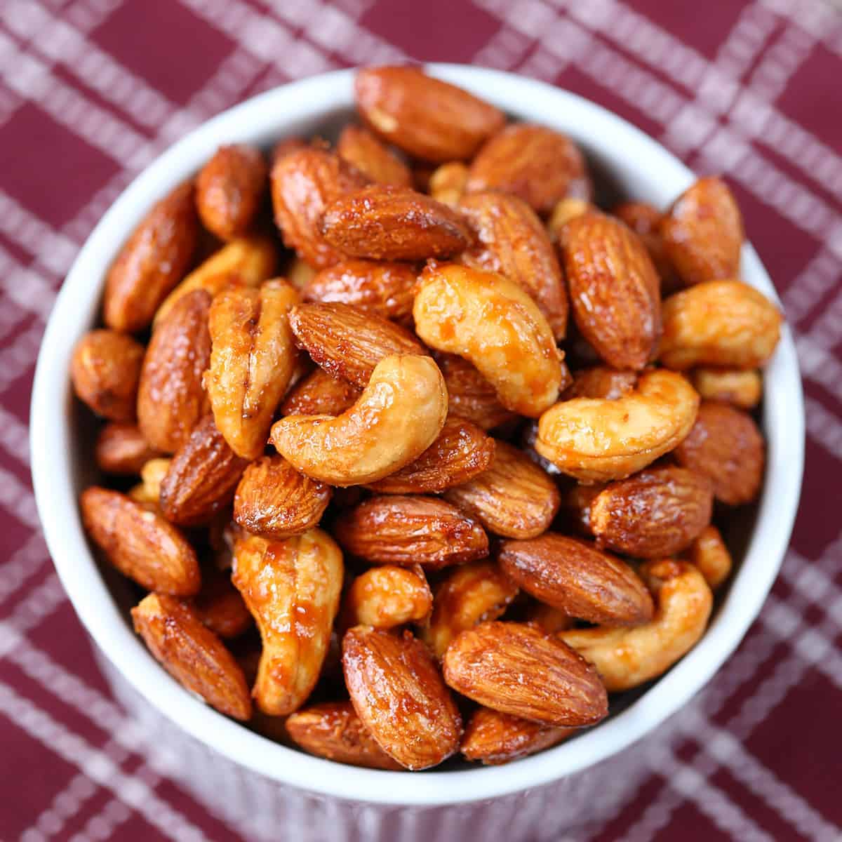 maple sriracha roasted nuts in a white ramekin on a burgundy and white kitchen towel.