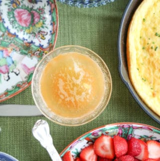 bellini in a coupe glass on a green tablecloth surrounded by brunch foods