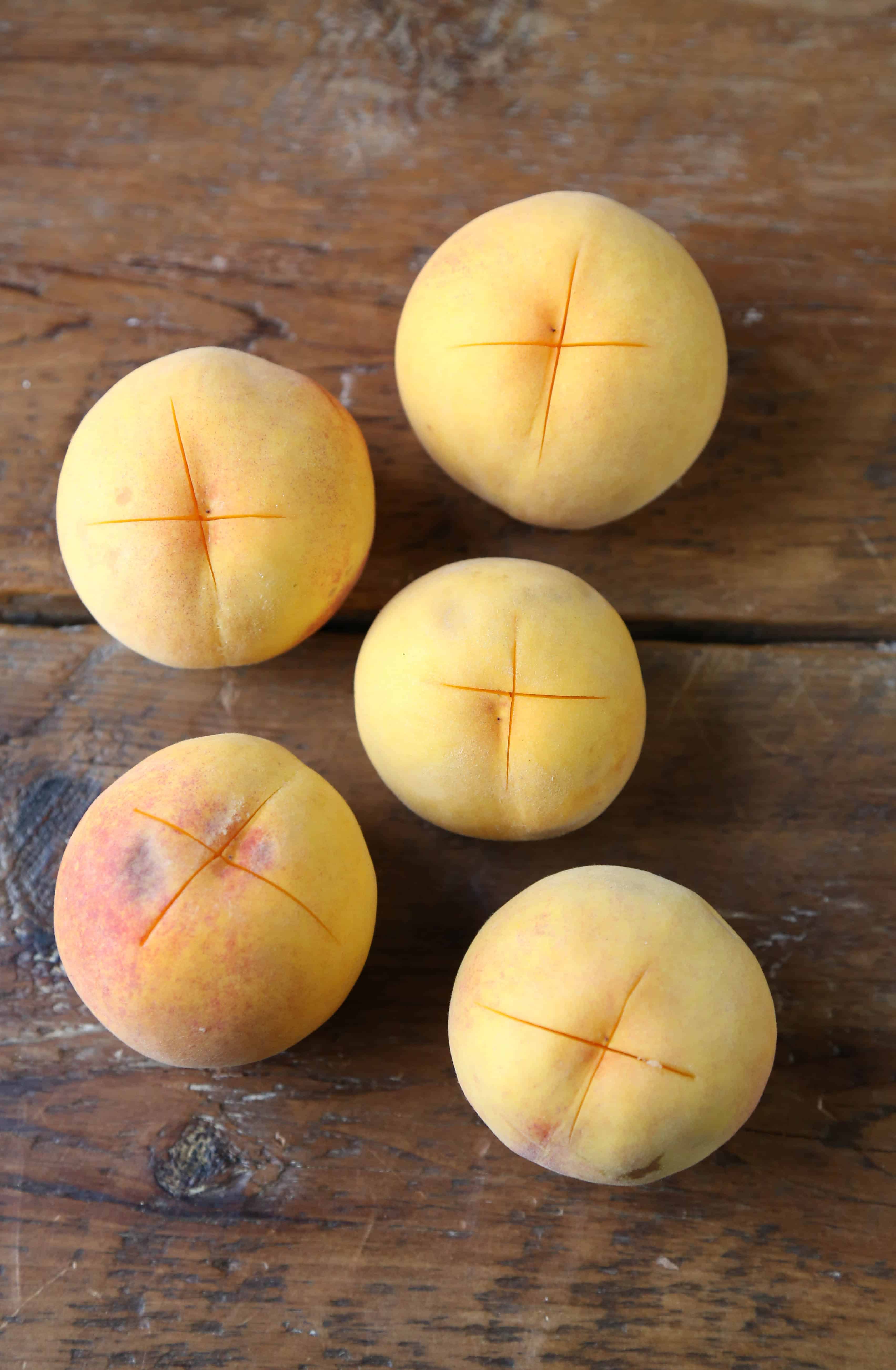 peaches with an "x" cut in the bottom on a wooden board