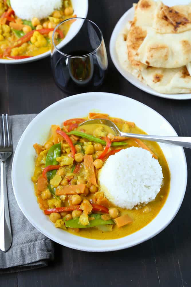 curry in a shallow white bowl with a side of rice on a dark wood table.