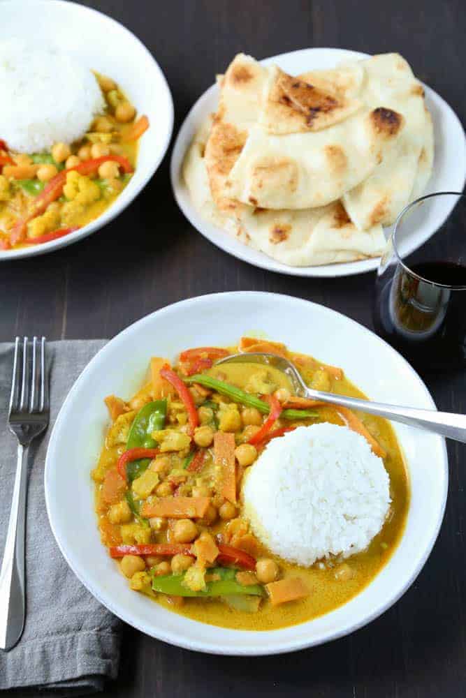 easy vegetarian curry in a shallow white bowl with a side of rice and a side of naan bread.