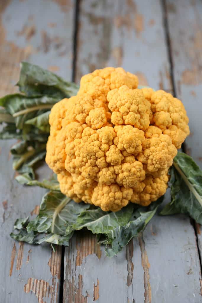 head of golden cauliflower with leaves on a blue wooden table.