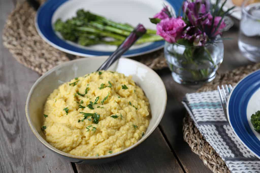 bowl of cauliflower mash on a table set for dinner with flowers and blue rimmed dinner plates.