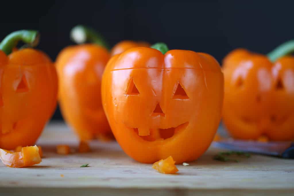 raw orange peppers with jack o'lanterns cut into them on a wooden board.