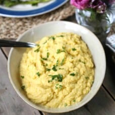 roasted garlic mashed cauliflower in a cream bowl with a spoon.