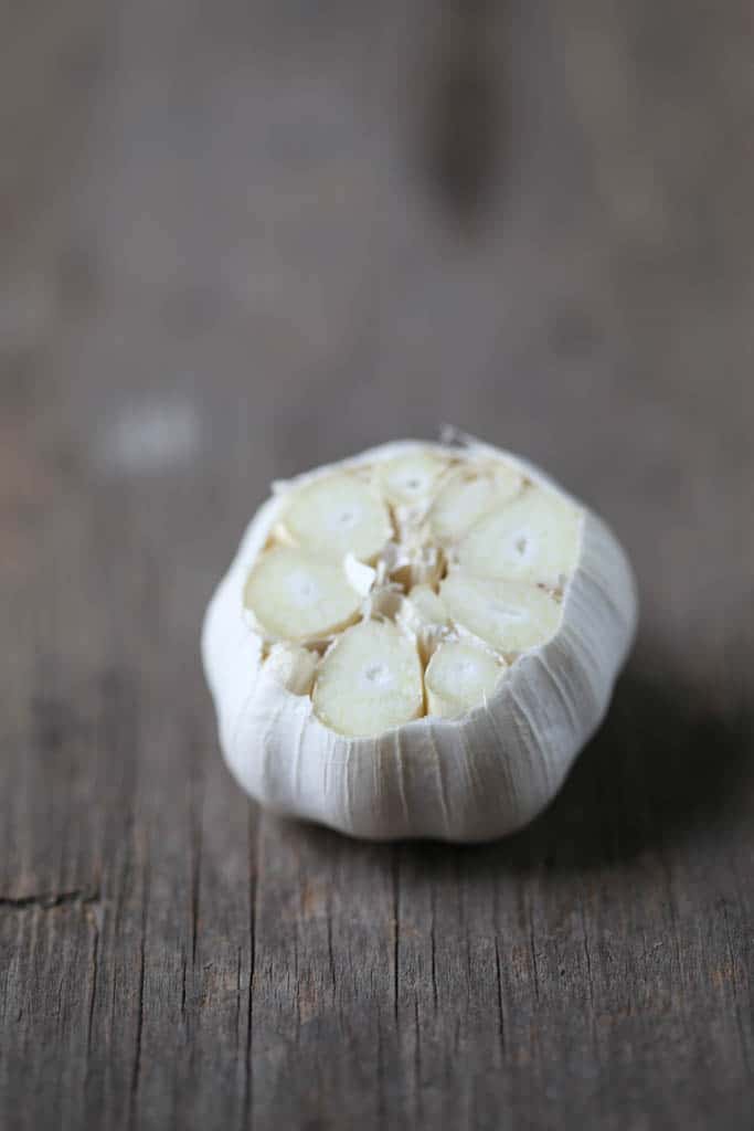 head of raw garlic with the top cut off on a wooden table.