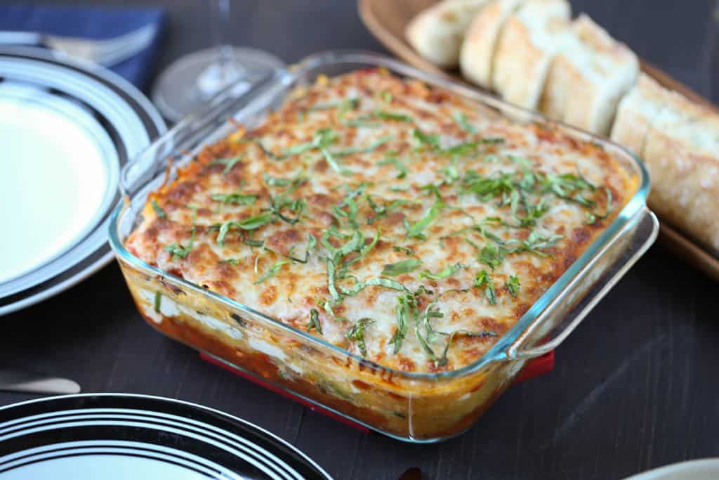 spaghetti squash lasagna on a wooden table with bread and plates.