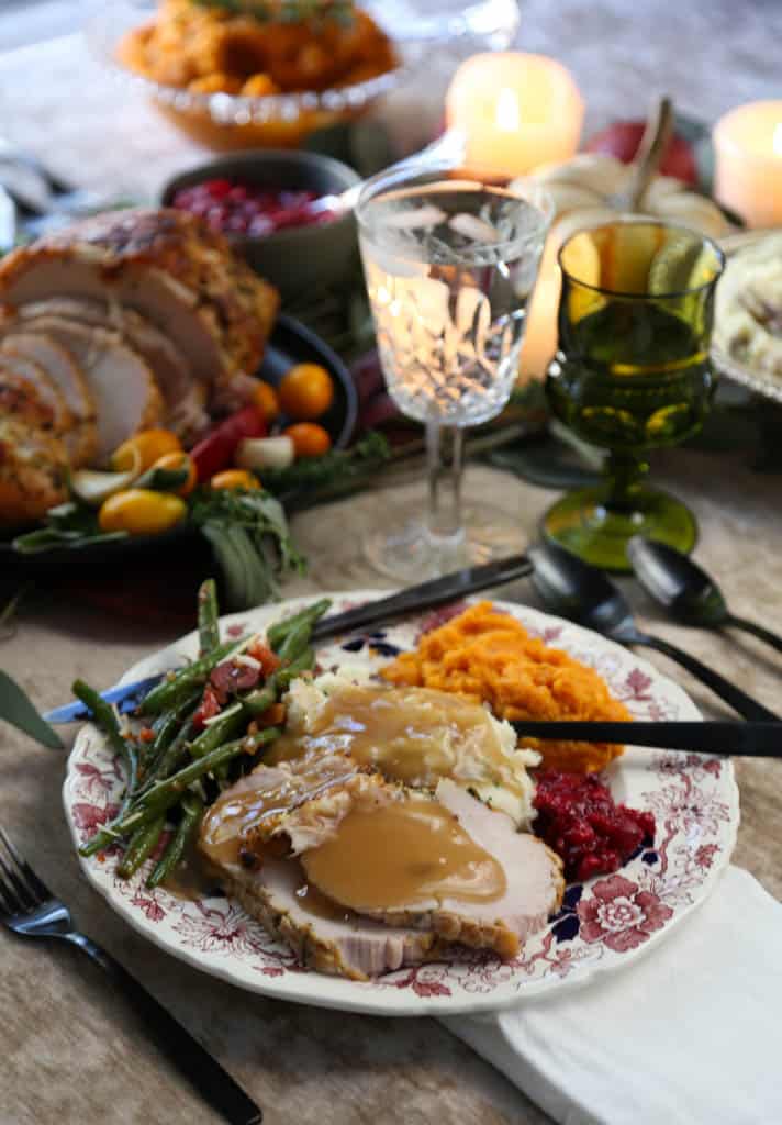dinner table set for Thanksgiving with a china plate filled with turkey, gravy, potatoes, and green beans.