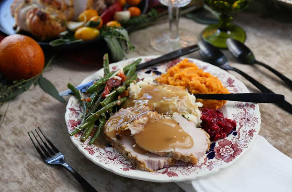 thanksgiving plate filled with sliced turkey, sweet potatoes, green beans, and cranberry sauce.
