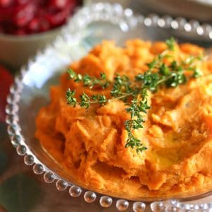 savory mashed sweet potatoes with fresh thyme on top in a glass bowl.
