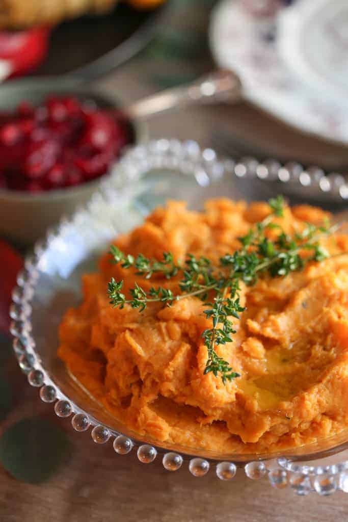 mashed sweet potatoes topped with fresh thyme in a decorative glass dish.