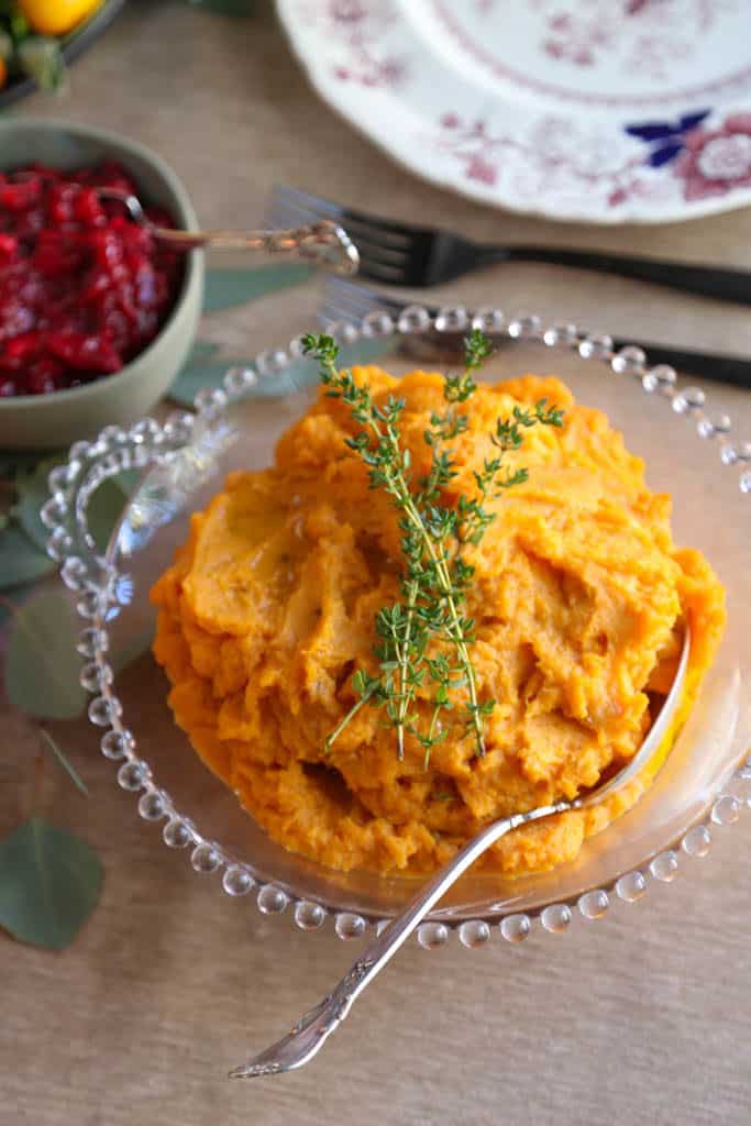 glass bowl of savory sweet potatoes topped with fresh thyme sprigs.