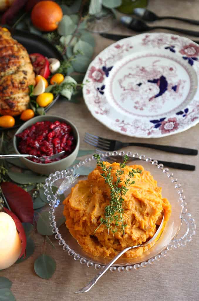 bowl of savory sweet potatoes on a thanksgiving table with cranberry sauce and china.